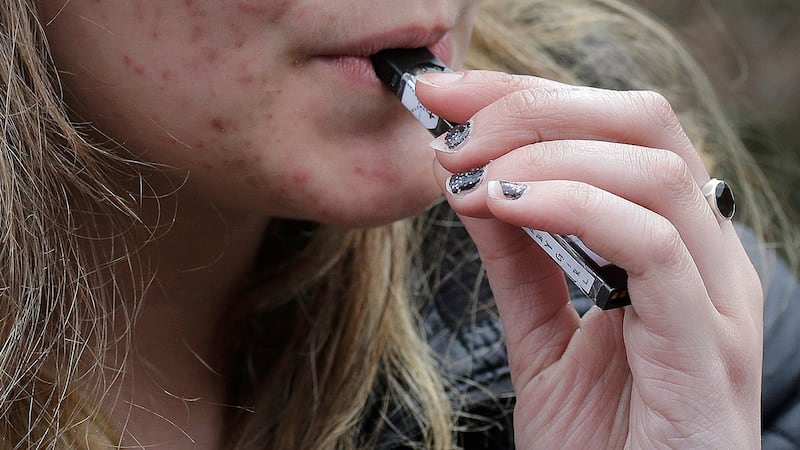 FILE - A high school student uses a vaping device near a school campus in Cambridge, Mass.,...
